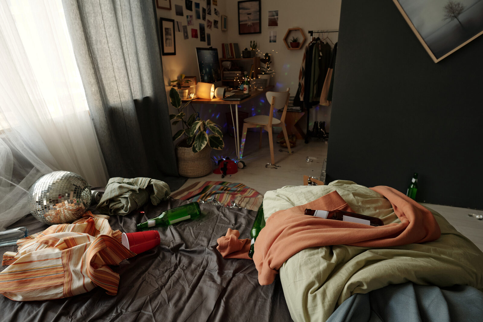 Une chambre laissée en désordre après une soirée : bouteilles, draps défaits, boule à facettes au sol